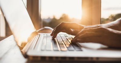 Person typing on a laptop with a sunset in the background